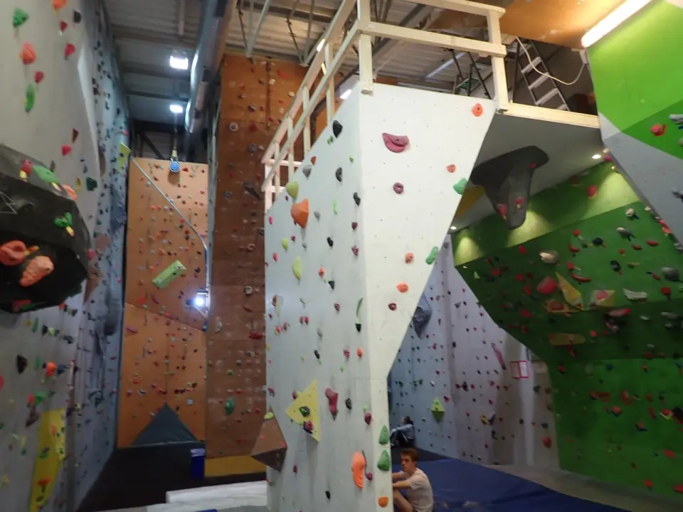 Climbing hall with tall orange and white rope walls beside a green overhanging wall