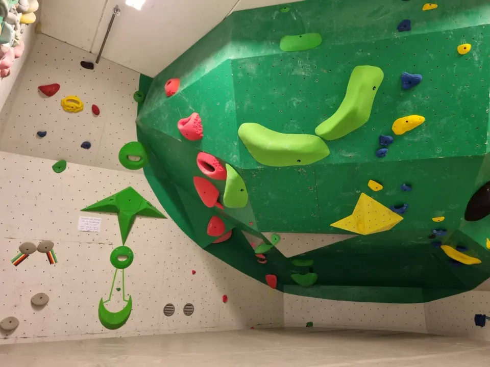 Bouldering room with a large overhanging green feature and a white side wall