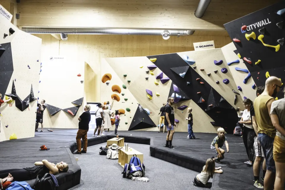 Bouldering hall with black and plywood walls and climbers on the padded floor