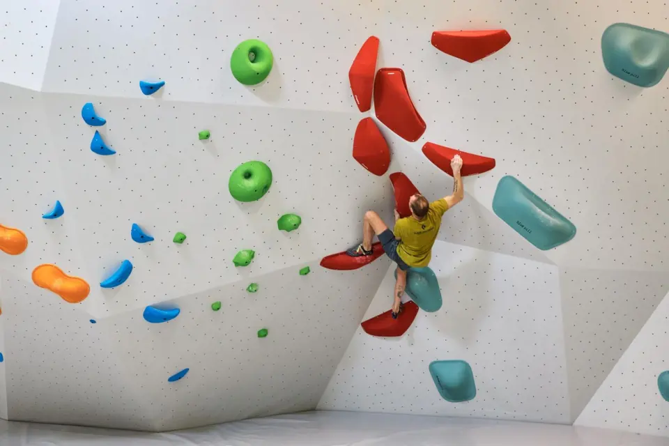 Boulderer reaching between large red volumes on a white wall