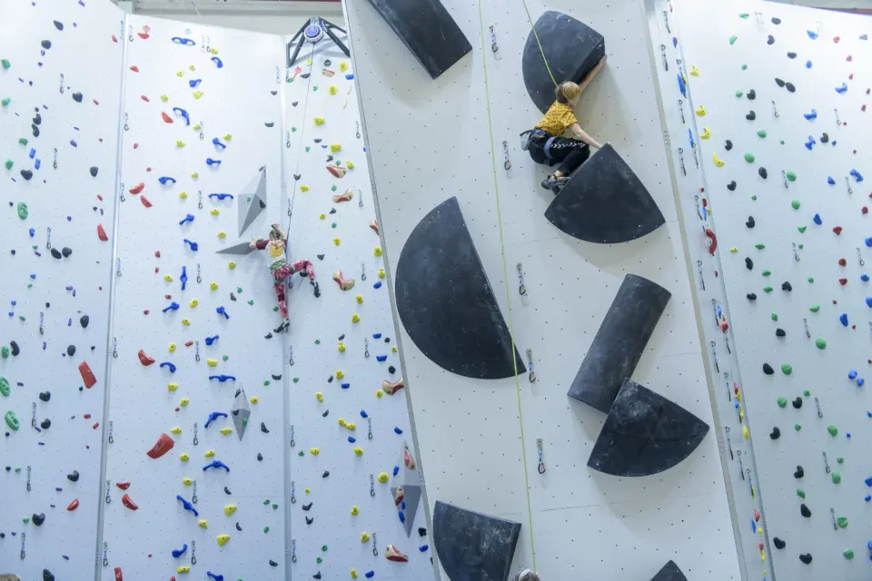 Two climbers on tall white rope walls with large black volumes