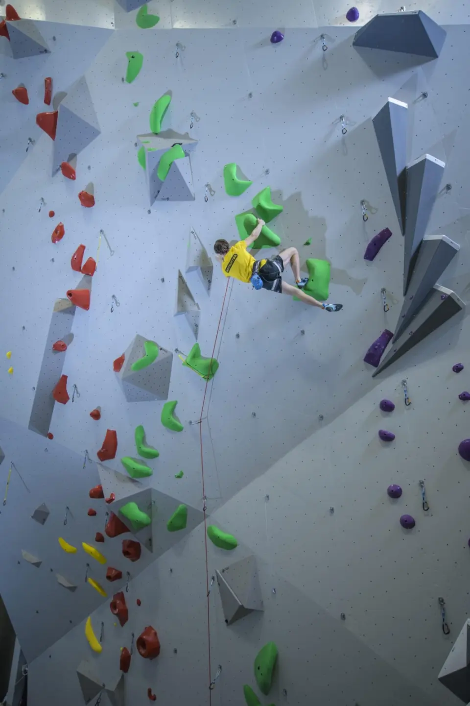 Lead climber high on a grey wall with jutting volumes