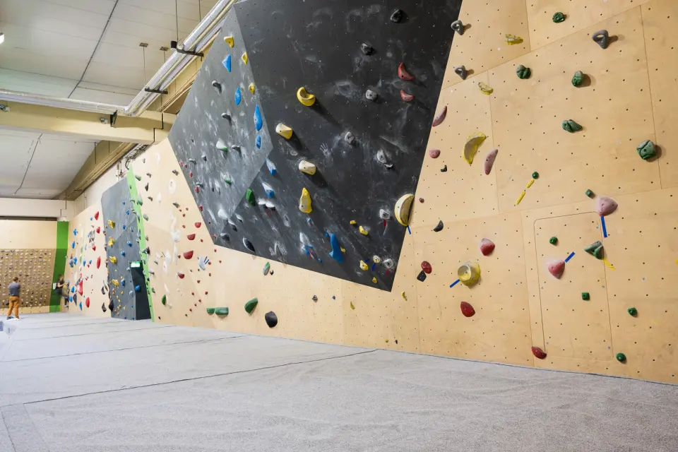 Long bouldering wall with grey and plywood panels above thick matting