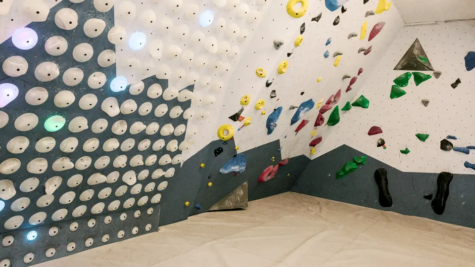 Bouldering room with an LED system board beside walls of coloured holds above white matting