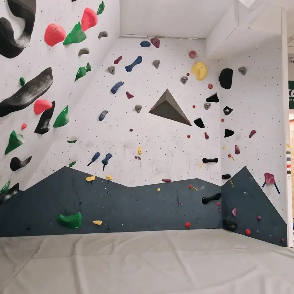 Corner of a bouldering wall with red, green and black holds and a triangular volume