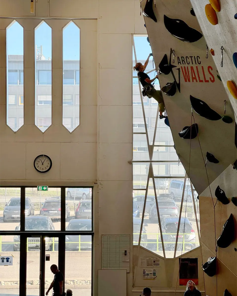 Lead climber on a steep overhanging wall beside tall hall windows