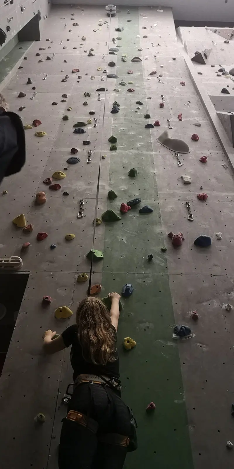 Looking up a tall roped wall from behind a climber at the start of a route