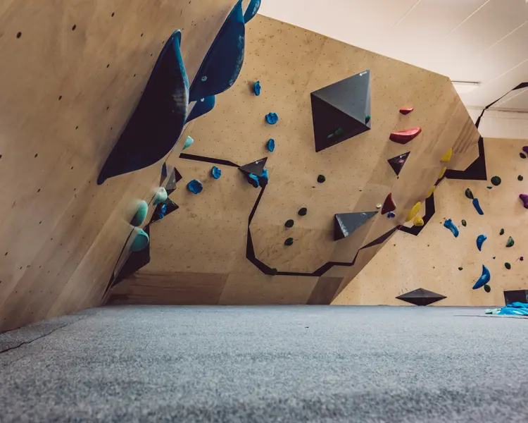 Plywood bouldering walls with black stripes, angular volumes and blue, red and yellow holds over grey matting