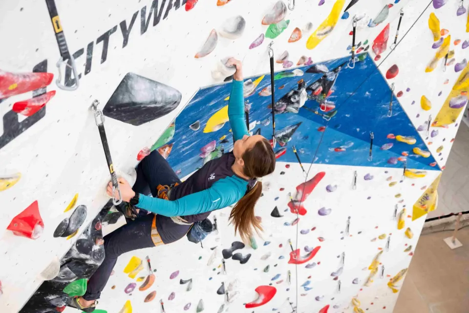 Lead climber clipping quickdraws on a white wall with a blue overhang