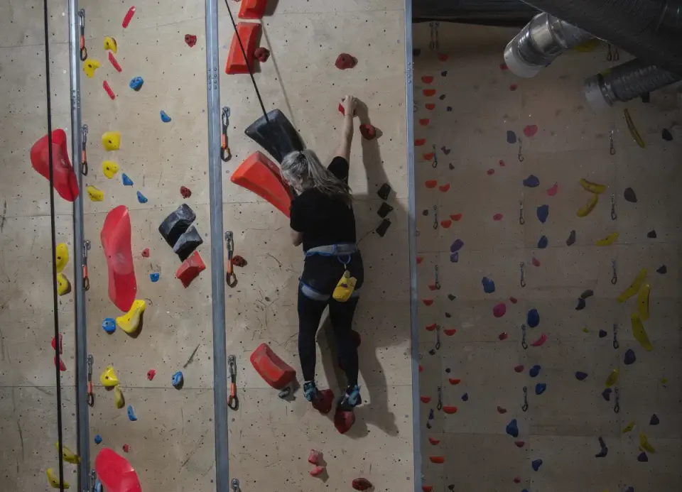 Climber on an auto-belay route on a tall wall with red, yellow and black holds