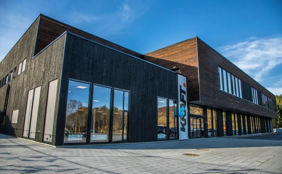Dark timber-clad sports centre with tall windows and a KRAFT sign by the entrance