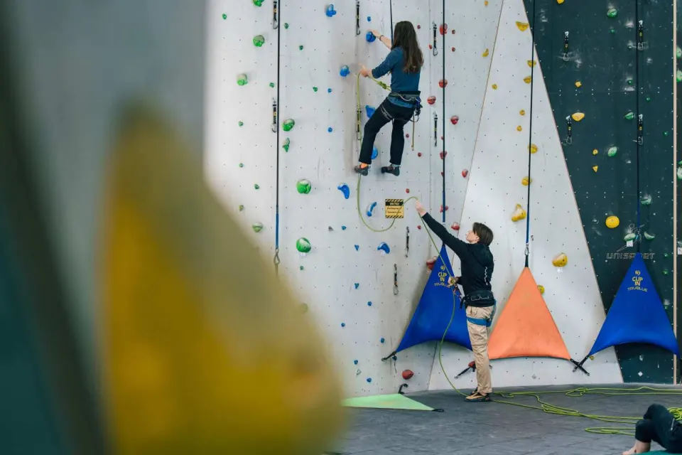 Climber on a rope route up the tall wall, with a belayer below
