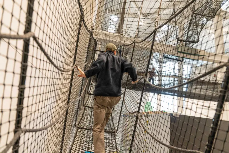 Visitor crossing the rope net park high above the trampoline hall