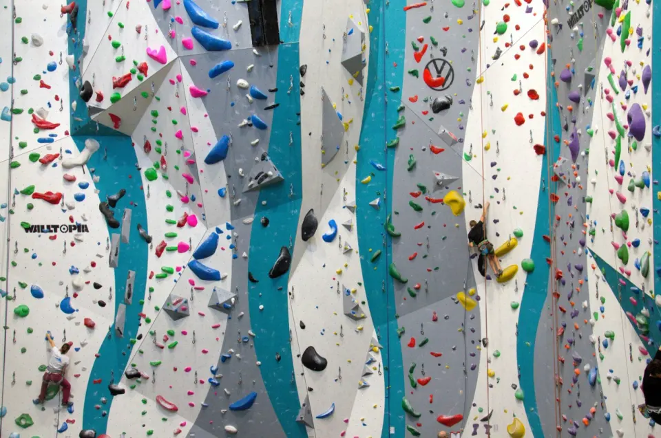 Tall rope walls covered in colourful routes, with two climbers part-way up