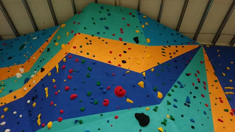 Tall climbing wall in blue, green and orange panels covered in coloured holds