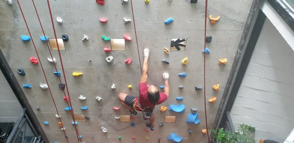 Climber seen from above on a grey top-rope wall with colourful holds and ropes