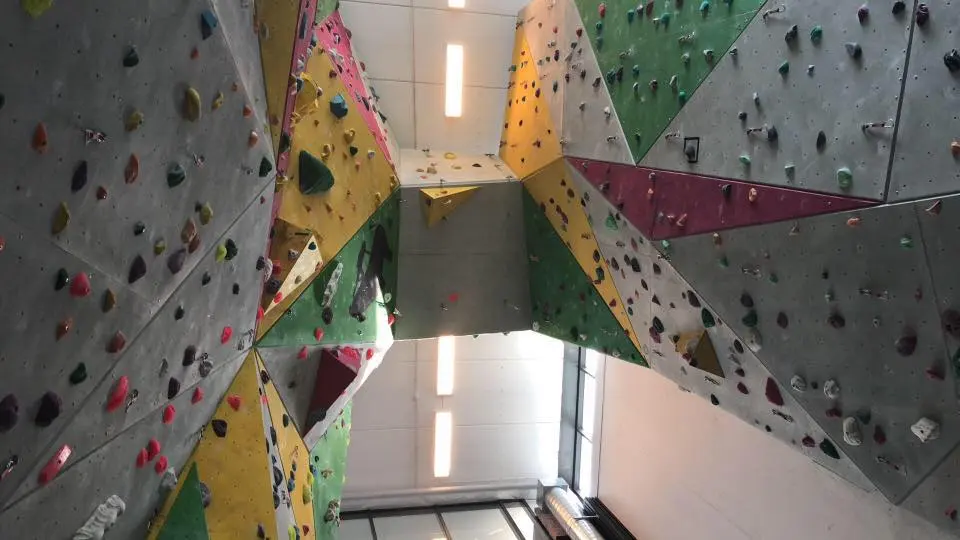 Looking up between tall climbing walls with grey, yellow, green and red panels