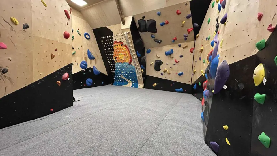 Bouldering room with plywood and black walls, grey matting and an LED board at the far end