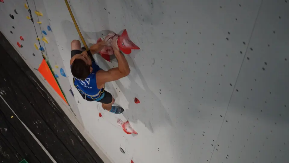 Climber racing up the red holds of the speed wall