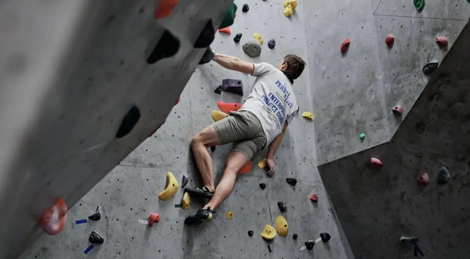 Climber on a grey climbing wall with colourful holds, seen from behind