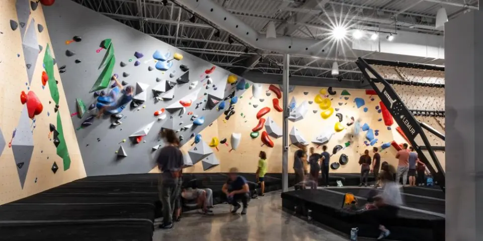 Bright bouldering hall with wooden and grey walls, deep matting and a training board on the right