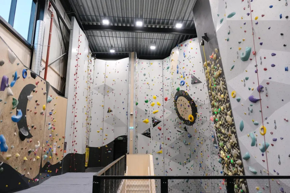 Tall rope walls with coloured holds beside a lit LED wall and a wooden bouldering wall