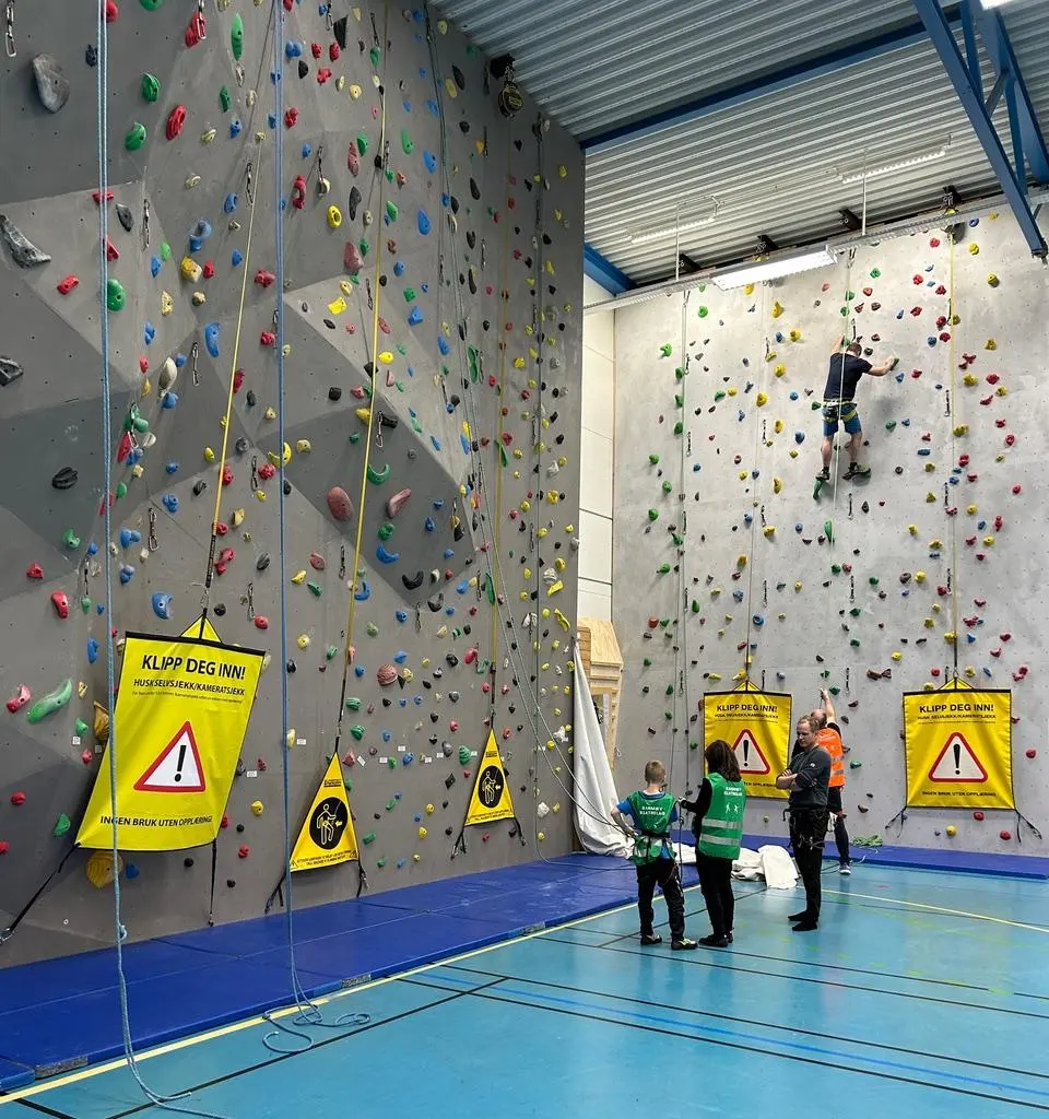 Two roped climbing walls with auto-belay warning flags and a climber halfway up the far wall
