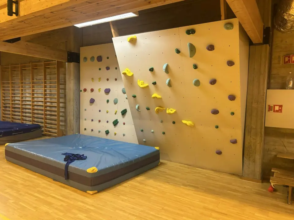 Bouldering wall with two angled panels above a thick crash mat in a wood-panelled hall