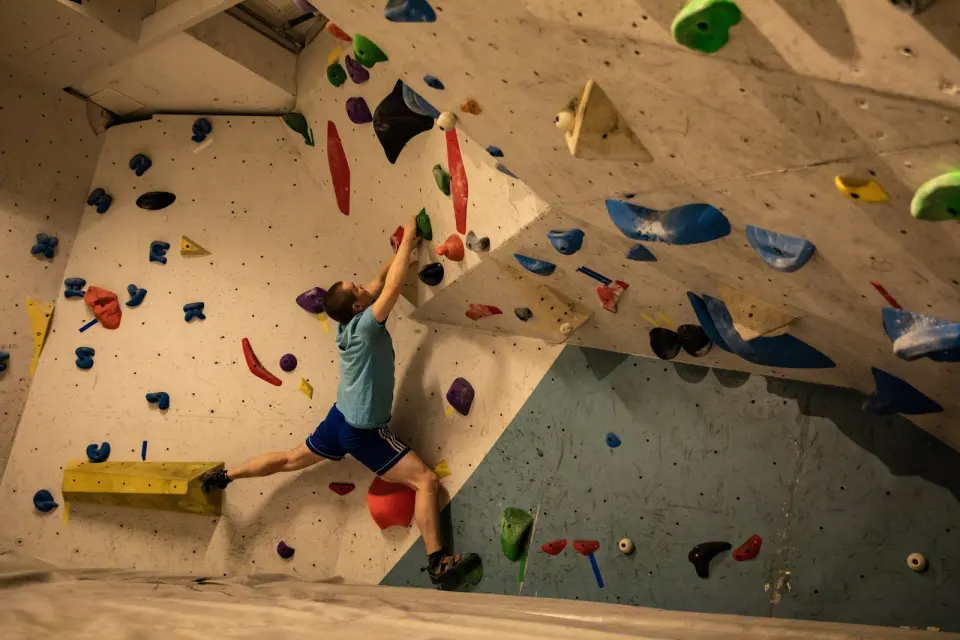 Climber reaching across a bouldering wall with an overhang and coloured holds