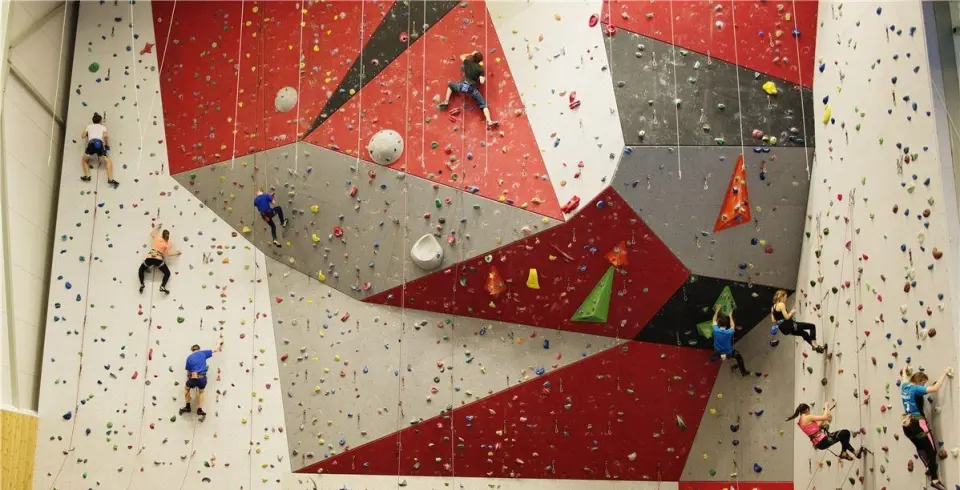 Climbers on ropes across the 15-metre wall with its red and grey overhanging panels