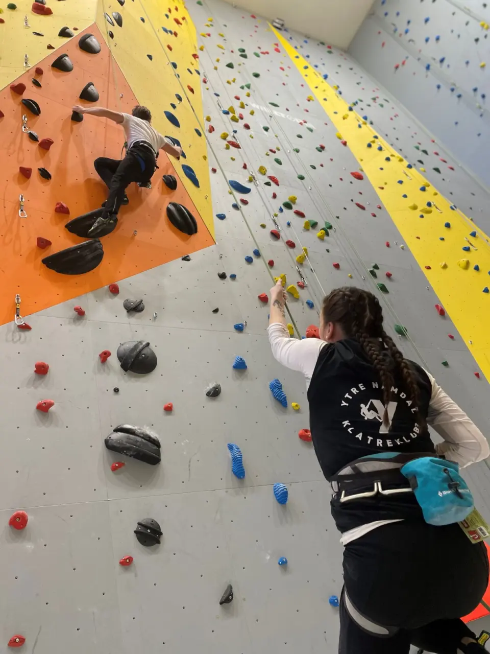 Climber on the orange overhang while another person points out holds from below