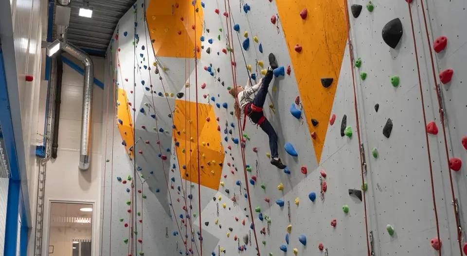 Young climber on a roped route on the grey and orange climbing wall