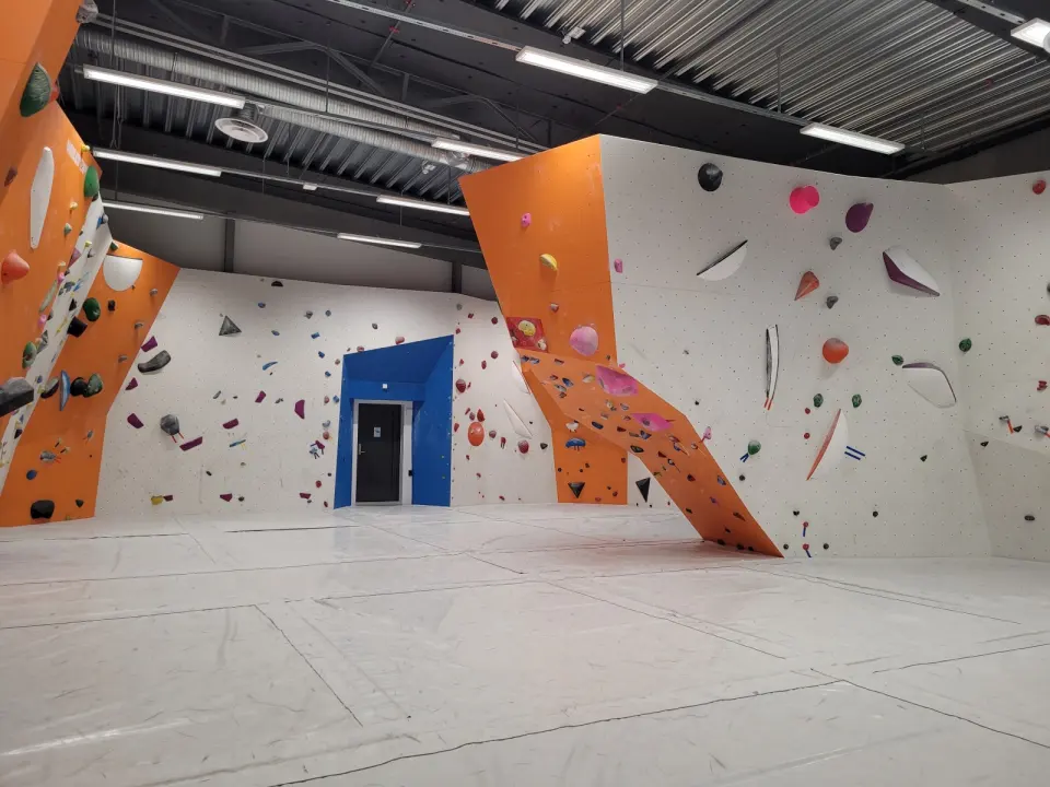 Bouldering room with orange and white angled walls above a fully matted floor