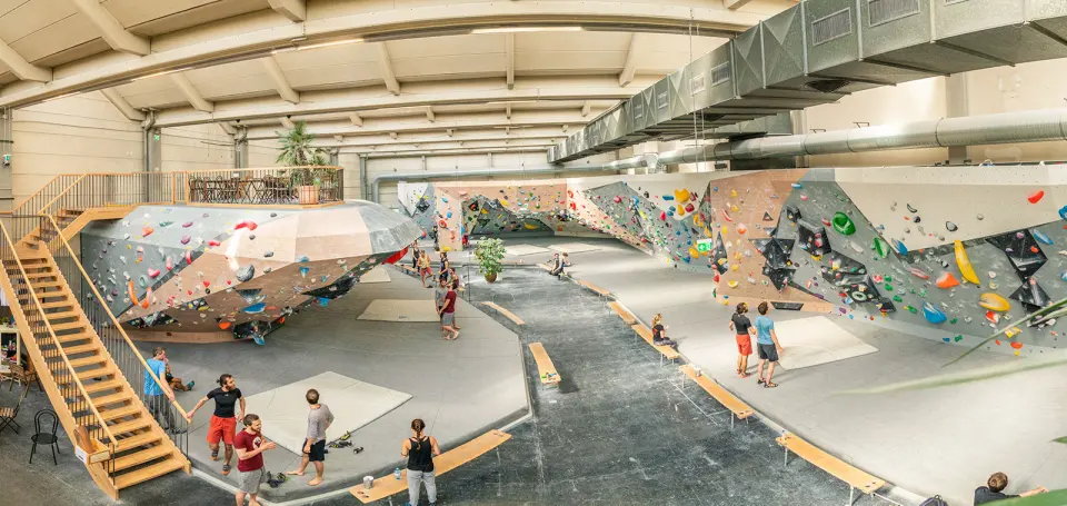 Bright bouldering hall seen from above, with a staircase and rows of angled walls