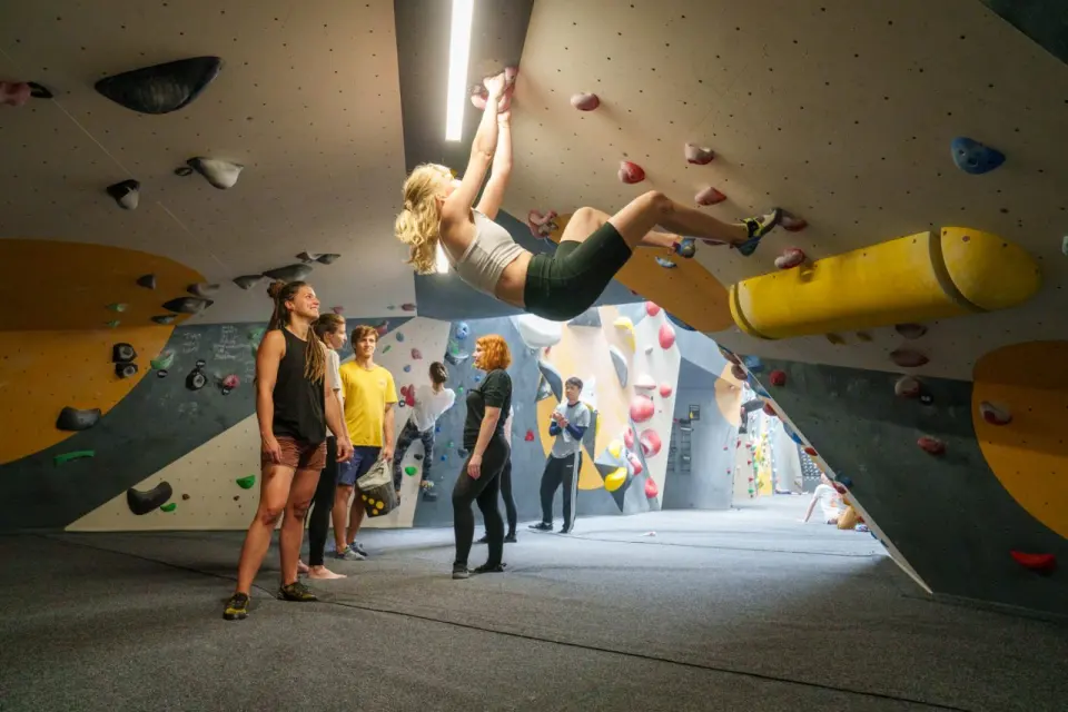 Climber on an overhang with others watching from the mats