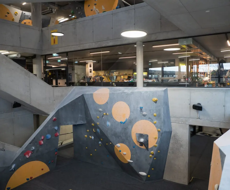Bouldering walls in a bright hall with a glazed gallery above