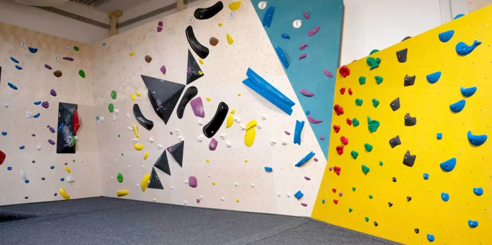 Bouldering walls in white, teal and yellow with colourful holds and volumes