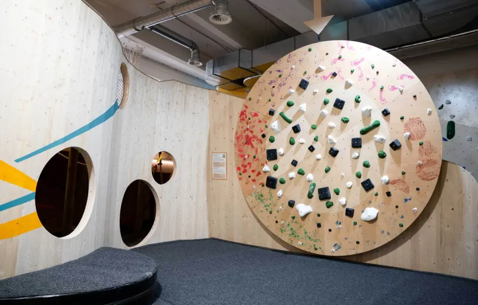 Large round climbing wall beside a wooden wall with porthole windows