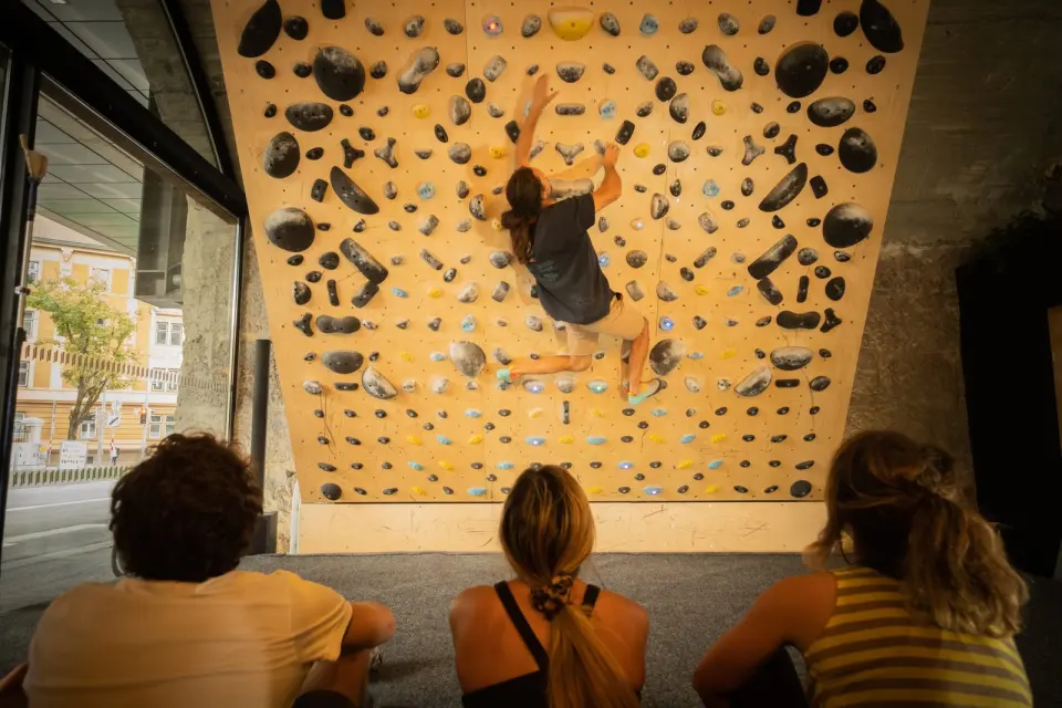 Climber on the angled training board while friends watch from the mats