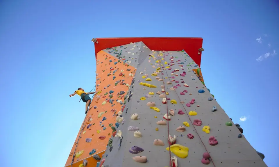Climber on the outdoor tower's orange and grey walls against a blue sky