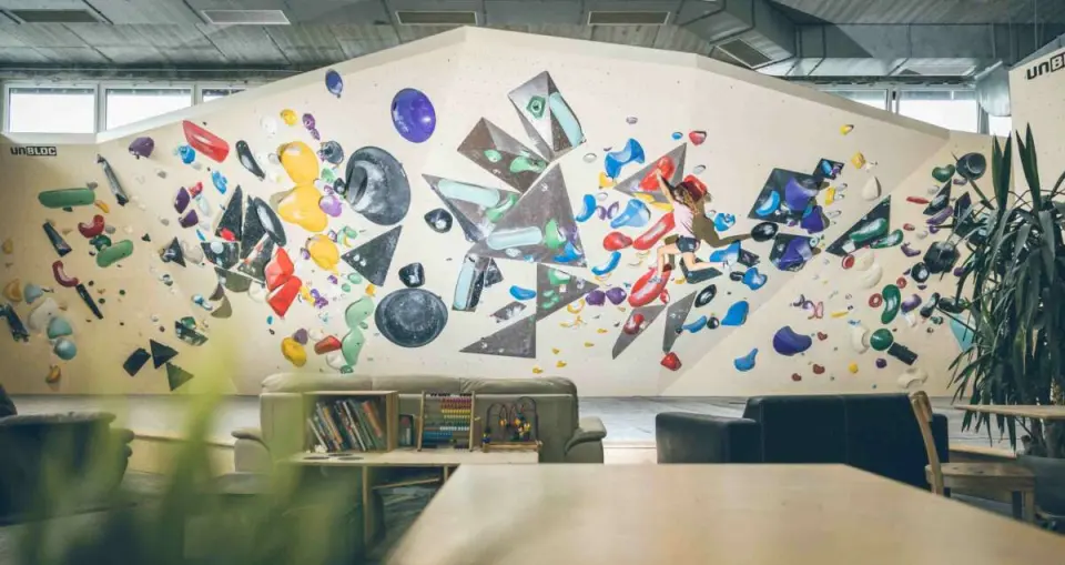 Climber on a wide bouldering wall above a lounge with sofas