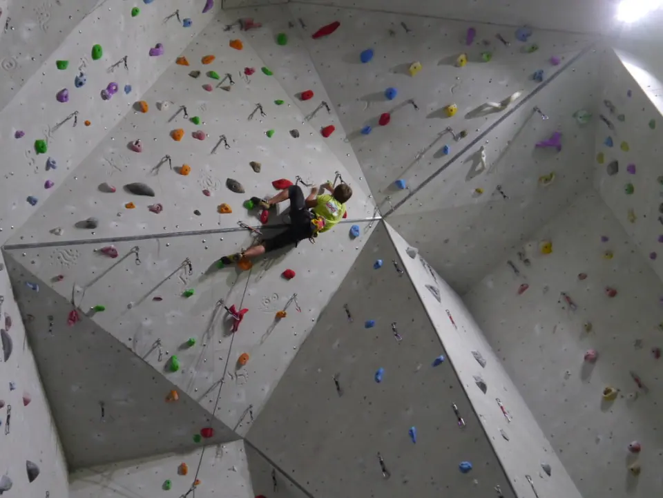 Climber high on an angular grey wall hung with quickdraws