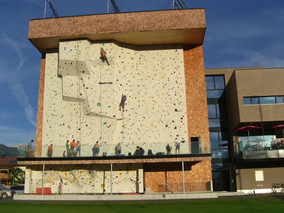 Climbers on the tall outdoor lead wall on the hall's façade, with a bouldering wall below