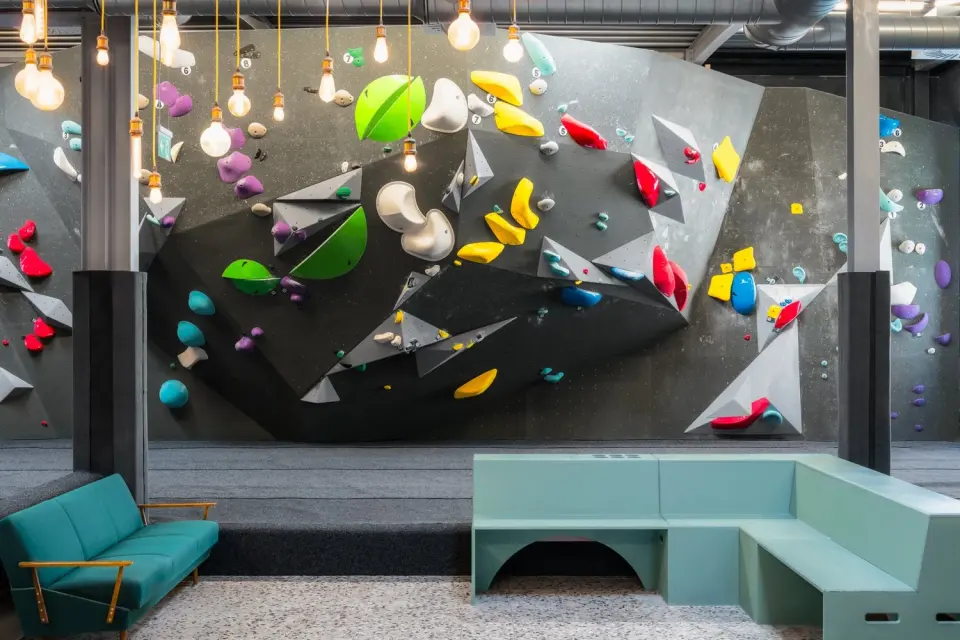 Steep grey bouldering wall with colourful holds above green benches