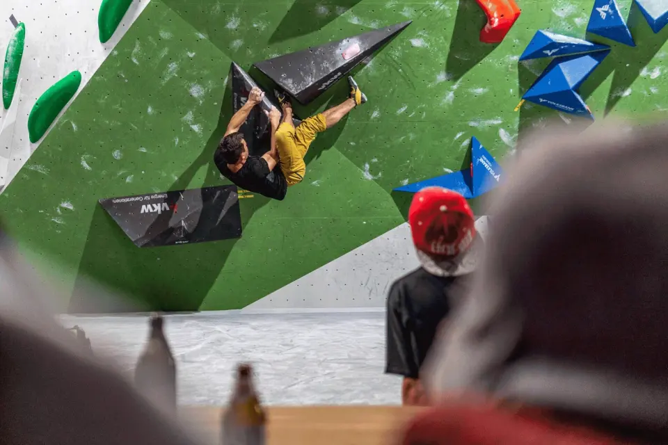 Climber on a steep green wall with black volumes during a competition
