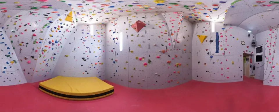 Panorama of a small climbing hall with holds on every wall and a crash mat