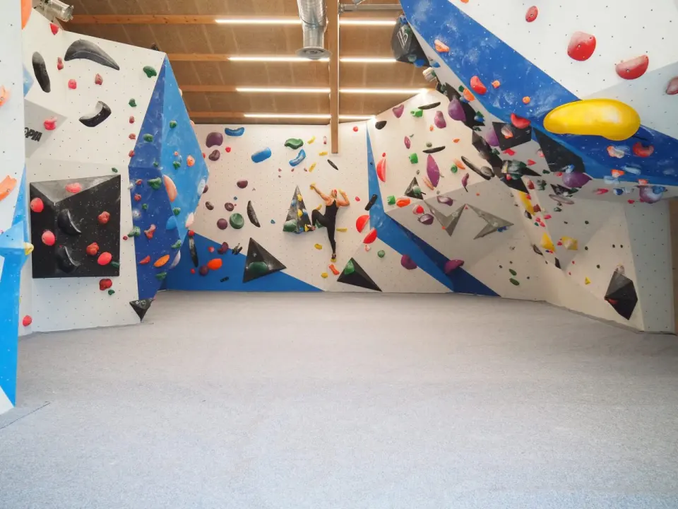 Bouldering hall with blue and white walls, steep overhangs and a grey matted floor