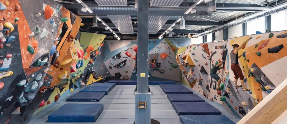 Bouldering hall with colourful painted walls on both sides and blue crash mats down the middle