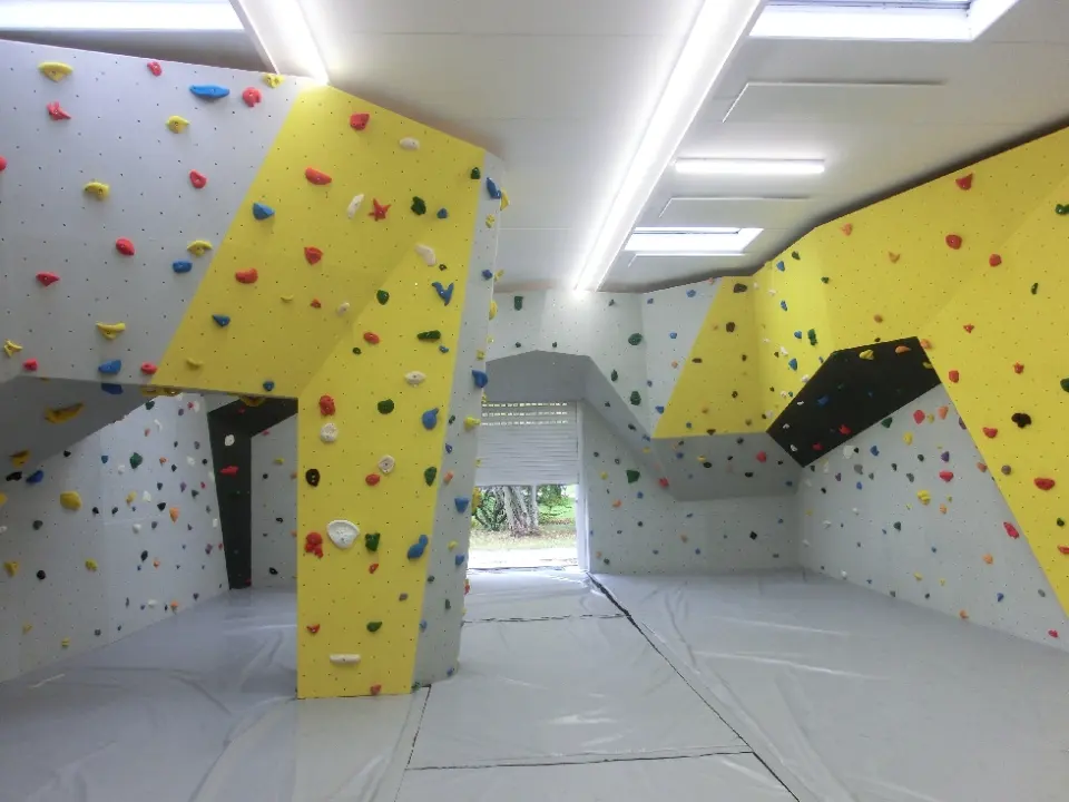 Bouldering hall with grey and yellow walls, overhangs and a free-standing pillar above grey mats