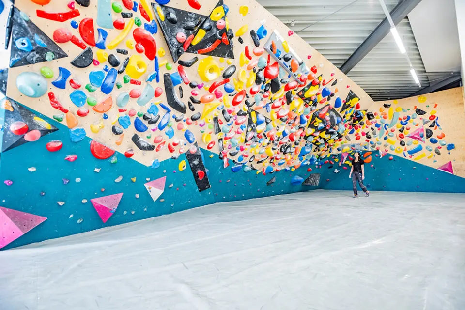 Long overhanging bouldering wall packed with colourful holds and volumes above grey mats
